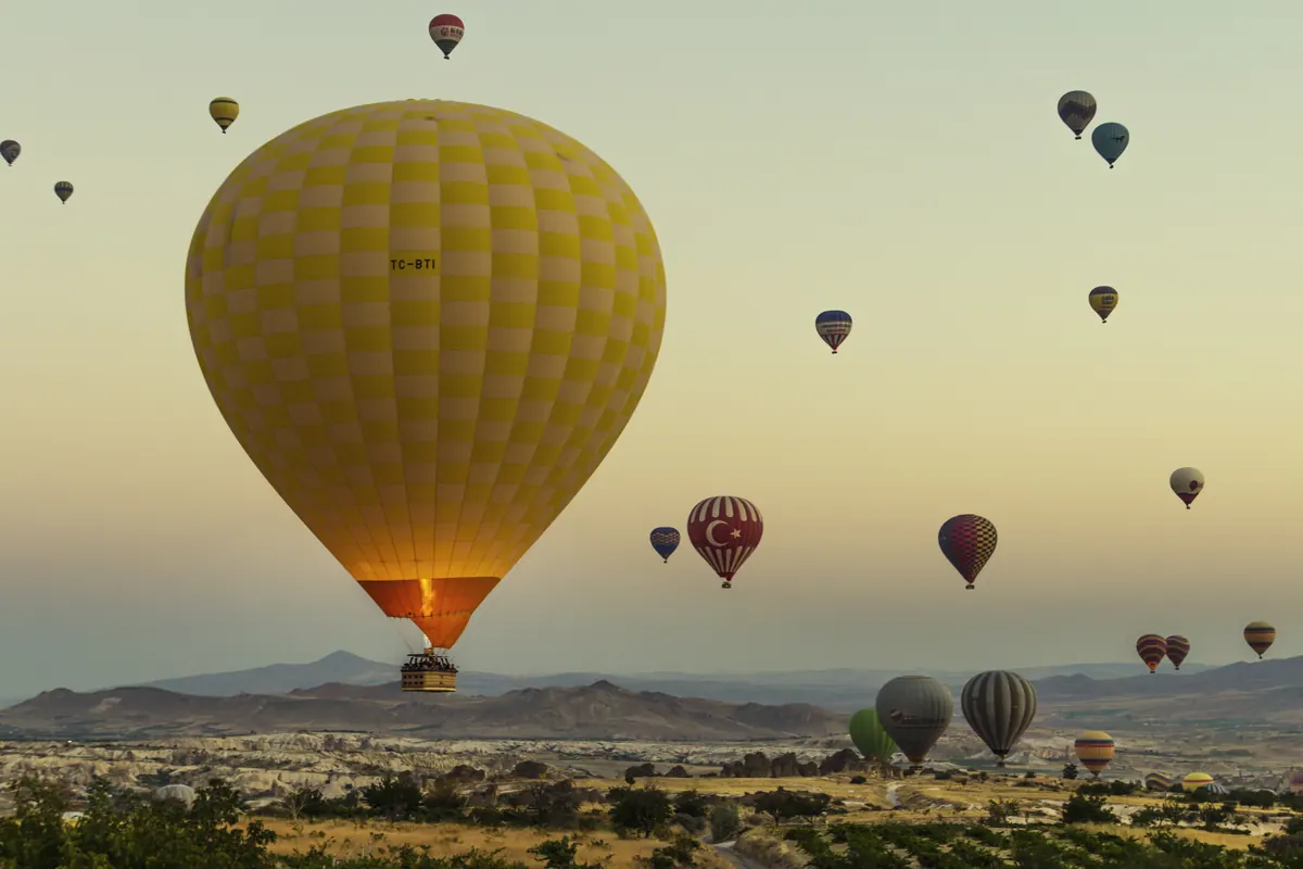 A hot air balloon rising at sunrise with many more balloons over Göreme