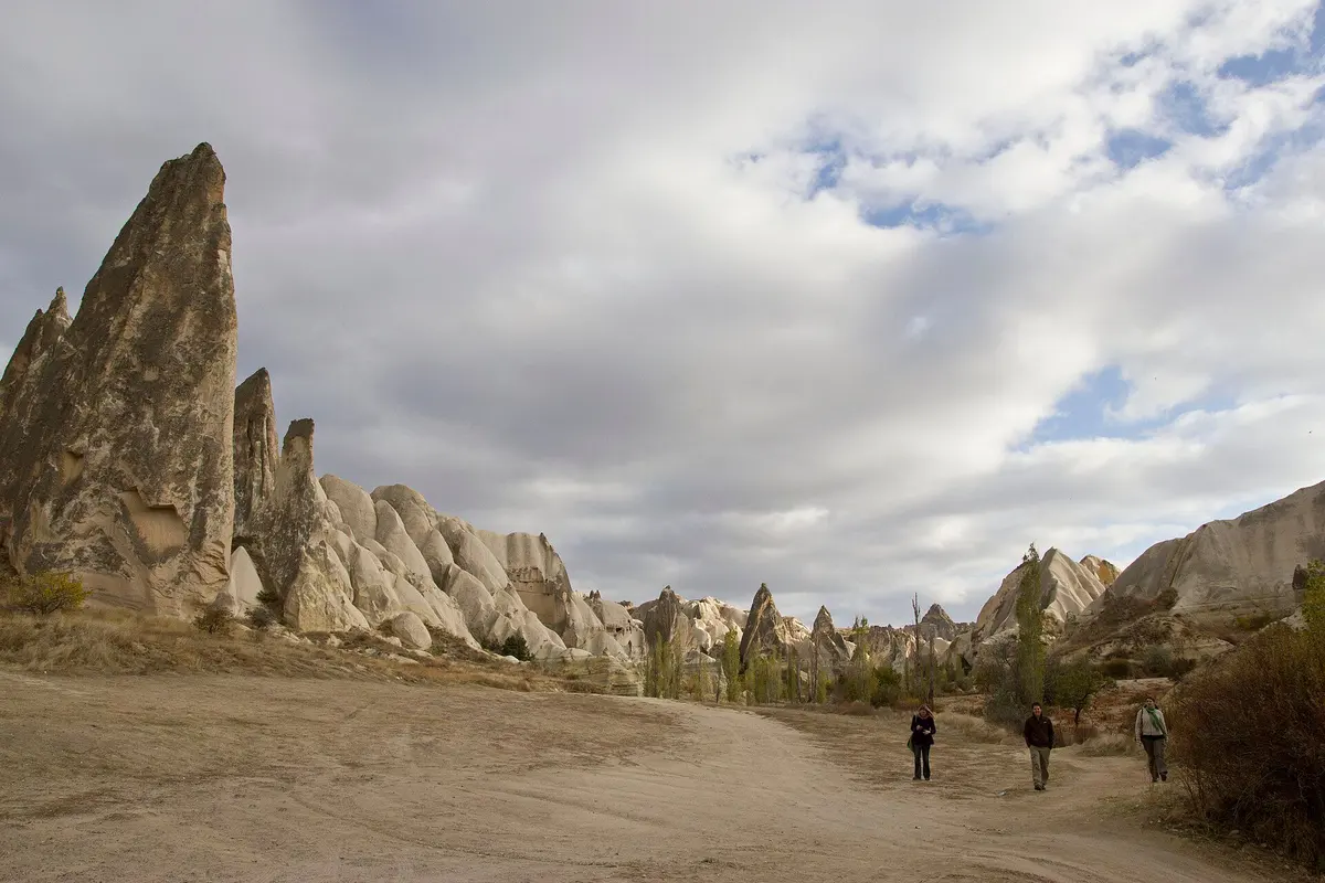 Pendaki di jalur berpasir Lembah Mawar di bawah menara batu yang tinggi, Cappadocia